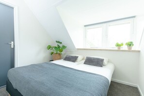 A bedroom with a bed, a window, and a potted plant.