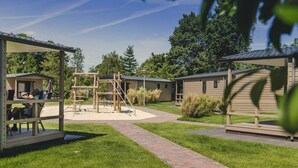 Een camping met houten hutten, een speeltuin en een overdekt zitgedeelte.