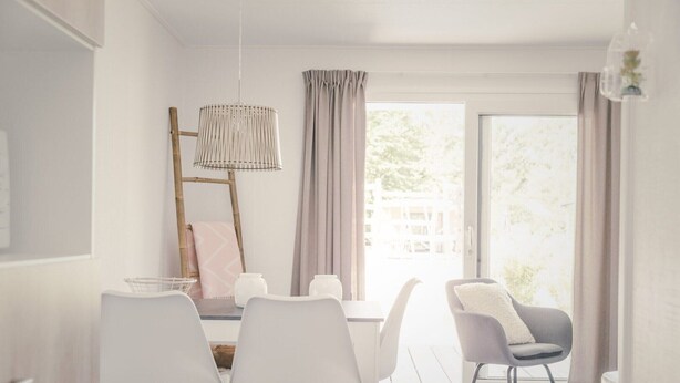 Een eethoek met een tafel, stoelen, een hanglamp en uitzicht door een raam.