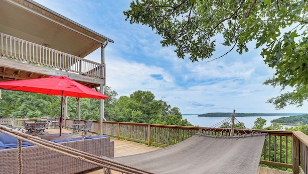 Una terraza de madera con mobiliario exterior, una hamaca y vistas a un lago.