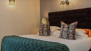 Una habitación de hotel con cabecera capitonada, manta tejida de color verde y almohadas con estampado floral.