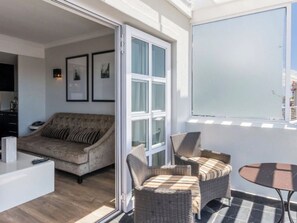 A modern living room with a sofa, wicker chairs, a coffee table, and a sliding glass door leading to a balcony. - Maximum 2 people and kids under 6 stay for free (Cape Town)