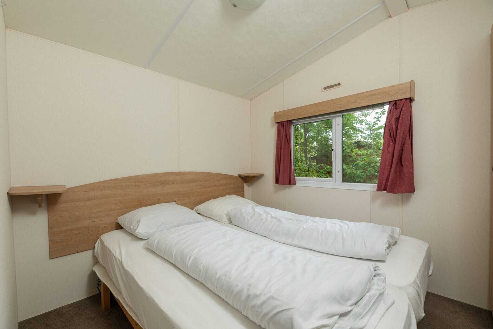 Een enkel bed met een houten hoofdbord, een raam met gordijnen en een plank boven het bed.
