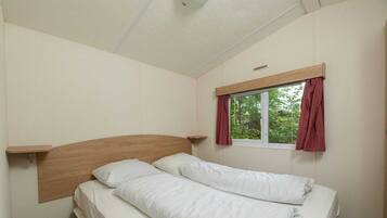 Een enkel bed met een houten hoofdbord, een raam met gordijnen en een plank boven het bed.
