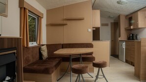 Ein gemütlicher Wohnbereich mit einer Couch, einem kleinen Tisch und Hockern, einer Küchenzeile und einem Fenster mit Vorhängen.