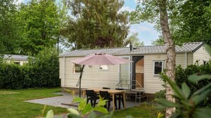 Ein Mobilheim mit Terrasse, Tisch und Stühlen im Freien.