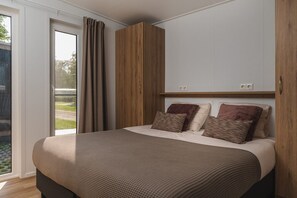 Een slaapkamer met een bed, gordijnen, een houten garderobe en uitzicht door een glazen deur.