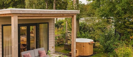 A wooden deck with a sofa and a hot tub in a lush garden setting.