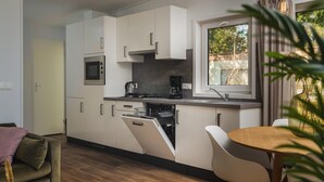 Une cuisine compacte avec des meubles blancs, un four encastré, une machine à café et une fenêtre donnant sur un jardin.