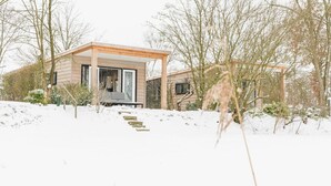 Une maison moderne avec une façade en bois, un porche abrité et un paysage enneigé.