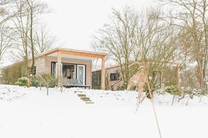 Een modern huis met een houten gevel, een overdekte veranda en een besneeerd landschap.