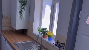 A compact kitchen with a sink, a washing machine, a window with plants, and a door. - Cozy 2-Bedroom Apartment in Tyne and Wear (Tyne and Wear)