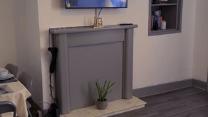 A living room with a fireplace, a flat-screen TV mounted above it, a small plant on the mantel, and a colorful rug on the floor. - Cozy 2-Bedroom Apartment in Tyne and Wear (Tyne and Wear)