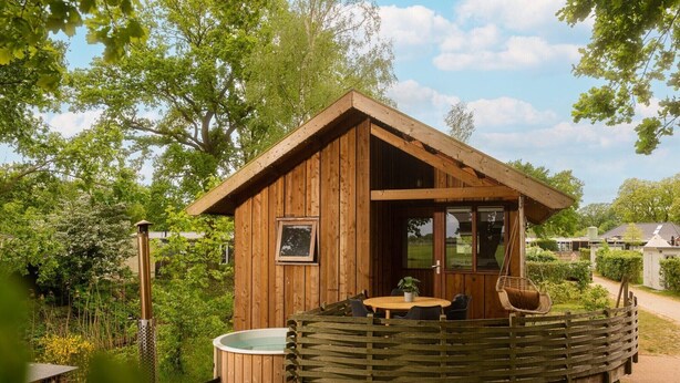 Een houten chalet met balkon, een jacuzzi en een eethoek.