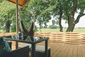 A wooden deck with wicker furniture, a hammock, and a view of a green landscape.