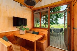 A wooden interior with a bench seating area, a table, a potted plant, and a television mounted on the wall.