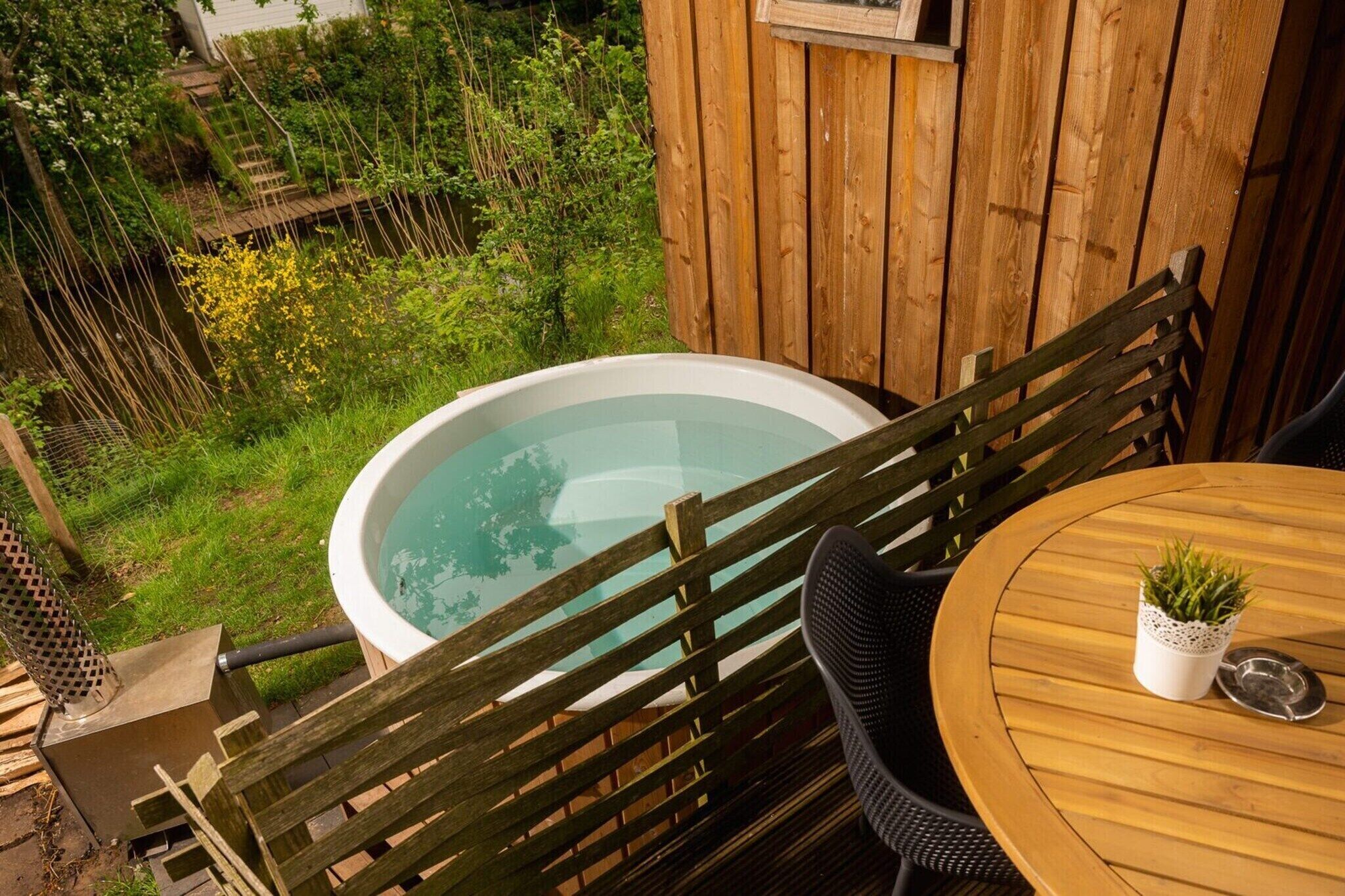 Een houten terras met een jacuzzi, een ronde houten tafel en een stoel.
