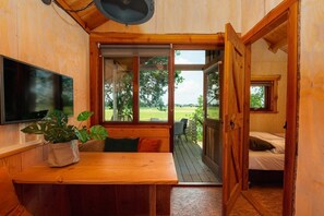 A wooden interior with a TV, a table with a plant, and a view of the outdoors.