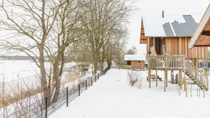 Een houten hut met een metalen dak, een houten terras en een pad bedekt met sneeuw.