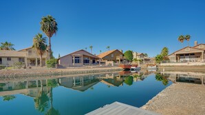 A waterfront property with a wooden deck, reflecting buildings and palm trees, and a calm water body. - Pool + Lakefront: Upscale Glendale Getaway (Glendale)