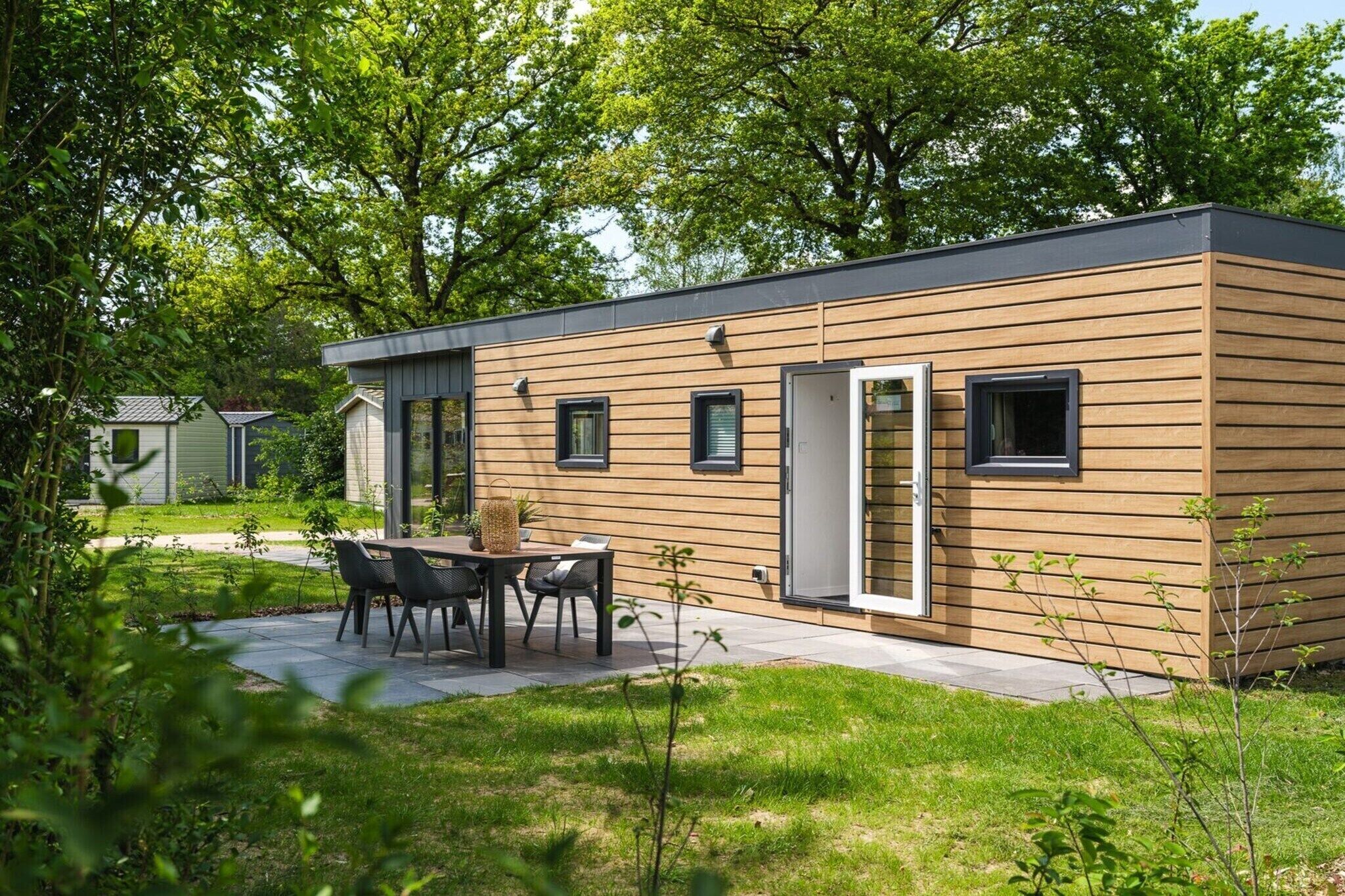 Ein modernes, eingeschossiges Gebäude mit Holzfassade, einer Terrasse mit Tisch und Stühlen sowie einer Tür, die zu einem Innenbereich führt.