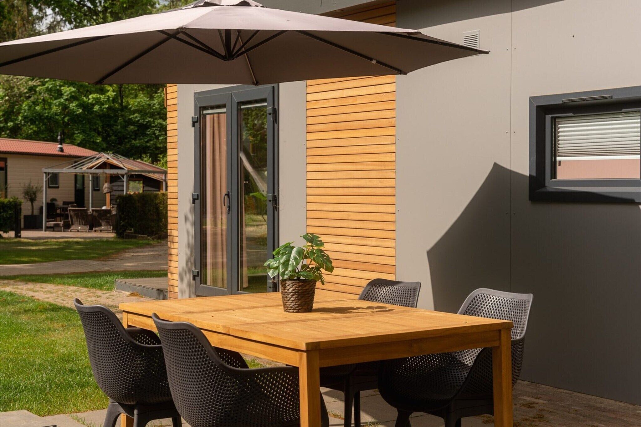 An outdoor patio with a wooden table and chairs, a potted plant, and a large umbrella.