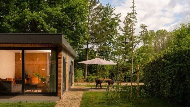 Et moderne hus med en glasdør, en terrasse med et bord og stole, samt en stor parasol.