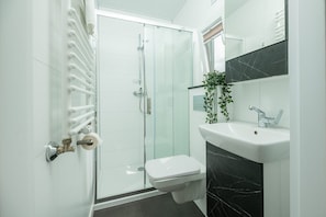 Een moderne badkamer met een douchecabine van glas, een wit toilet, een marmeren wastafel en een potplant.