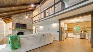 Un salón espacioso con chimenea de piedra, un sofá grande y una cocina al fondo.