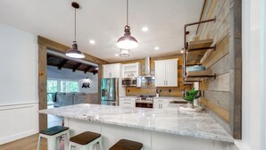 Una cocina moderna con isla de mármol, taburetes de bar, iluminación colgante y detalles de madera.