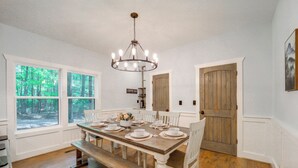 Un comedor con mesa de madera dispuesta para seis personas, sillas blancas, un banco e iluminación con candelabro.