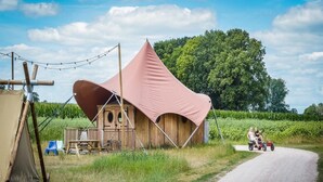Una estructura rústica de madera con un amplio dosel rosa, un camino de tierra y un tractor con dos personas.