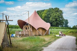 A rustic wooden structure with a large pink canopy, a dirt road, and a tractor with two people. - Glamping Oasis with Bohemian Flair (Zuna)