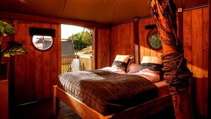 Un dormitorio de cabaña de madera con una cama, un ventanal circular y una cuerda colgando del techo.