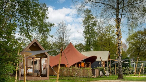 Una casa árbol con puerta de cristal, un pequeño porche y una estructura de techo rojo.