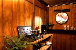 A kitchen with a stove, a pot, a coffee maker, and a round mirror on the wall. - Glamping Oasis with Bohemian Flair (Zuna)