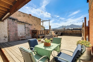 Una terraza de madera con mobiliario exterior, una mesa con mantel verde y una pared de ladrillo.