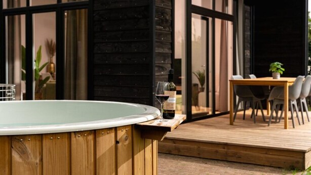 A wooden deck with a hot tub, a dining table with chairs, and a potted plant.