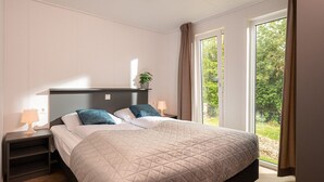 A bedroom with a bed, bedside tables, a nightstand, a window, and a view of greenery outside.