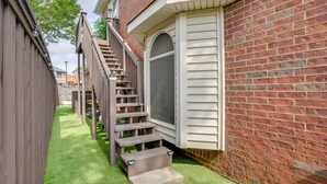 Una propiedad residencial con una escalera de madera que lleva a una puerta, un muro de ladrillo y un pequeño jardín delantero.