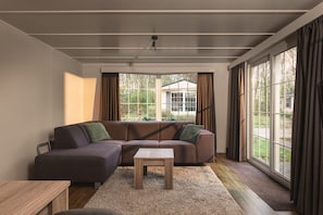 Una sala de estar moderna con un sofá modular, una mesita y ventanas amplias con cortinas.