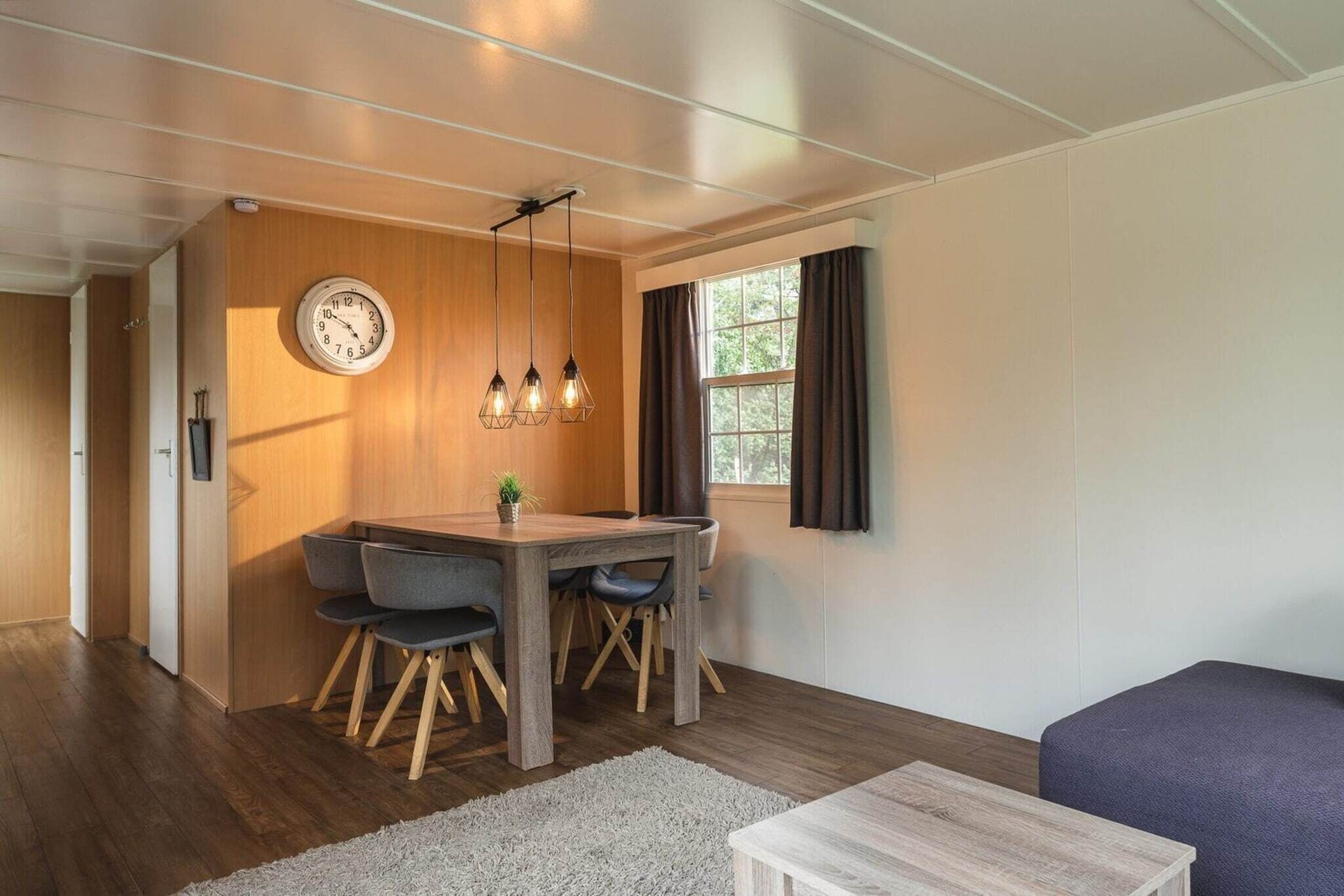 Een moderne kamer met een houten eettafel, stoelen, een klok en een raam met gordijnen.