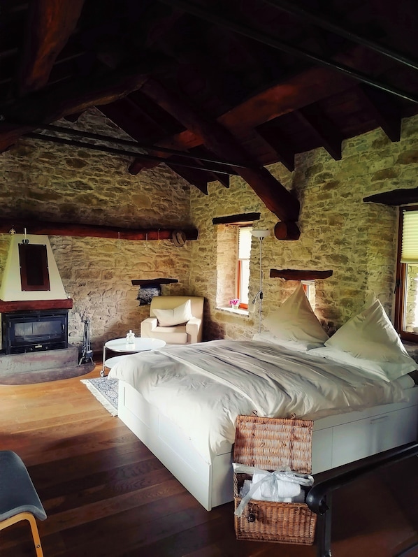 A bedroom with a stone wall, wooden beams, a bed, a chair, a small table, and a fireplace. - Charming Historic House in Provincia di Cuneo, Italia (Provincia di Cuneo)