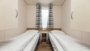 Een kamer met twee éénpersoonsbedden, een klein tafeltje en een raam met gordijnen met een patroon.