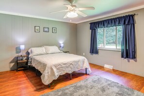 Une chambre à coucher comprenant un lit, des tables de chevet, un ventilateur de plafond, une fenêtre avec des rideaux et un mur orné de tableaux.
