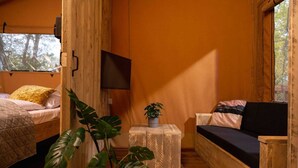Acogedor interior de cabaña con cama, sofá, televisor y planta en maceta.