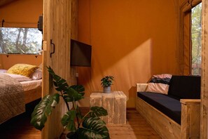 L’intérieur d’un chalet confortable, avec un lit, un canapé, une télévision et une plante en pot.