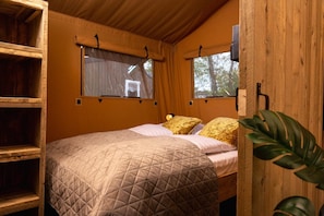 Une pièce en bois avec un lit, deux fenêtres avec des rideaux, une étagère et une plante.