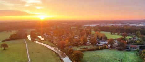 An aerial view of a rural area with fields, a river, and houses during sunset.