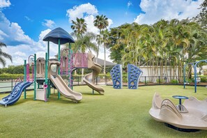Ein Spielplatz mit Rutschen und Klettergerüsten, umgeben von Palmen und blauem Himmel.